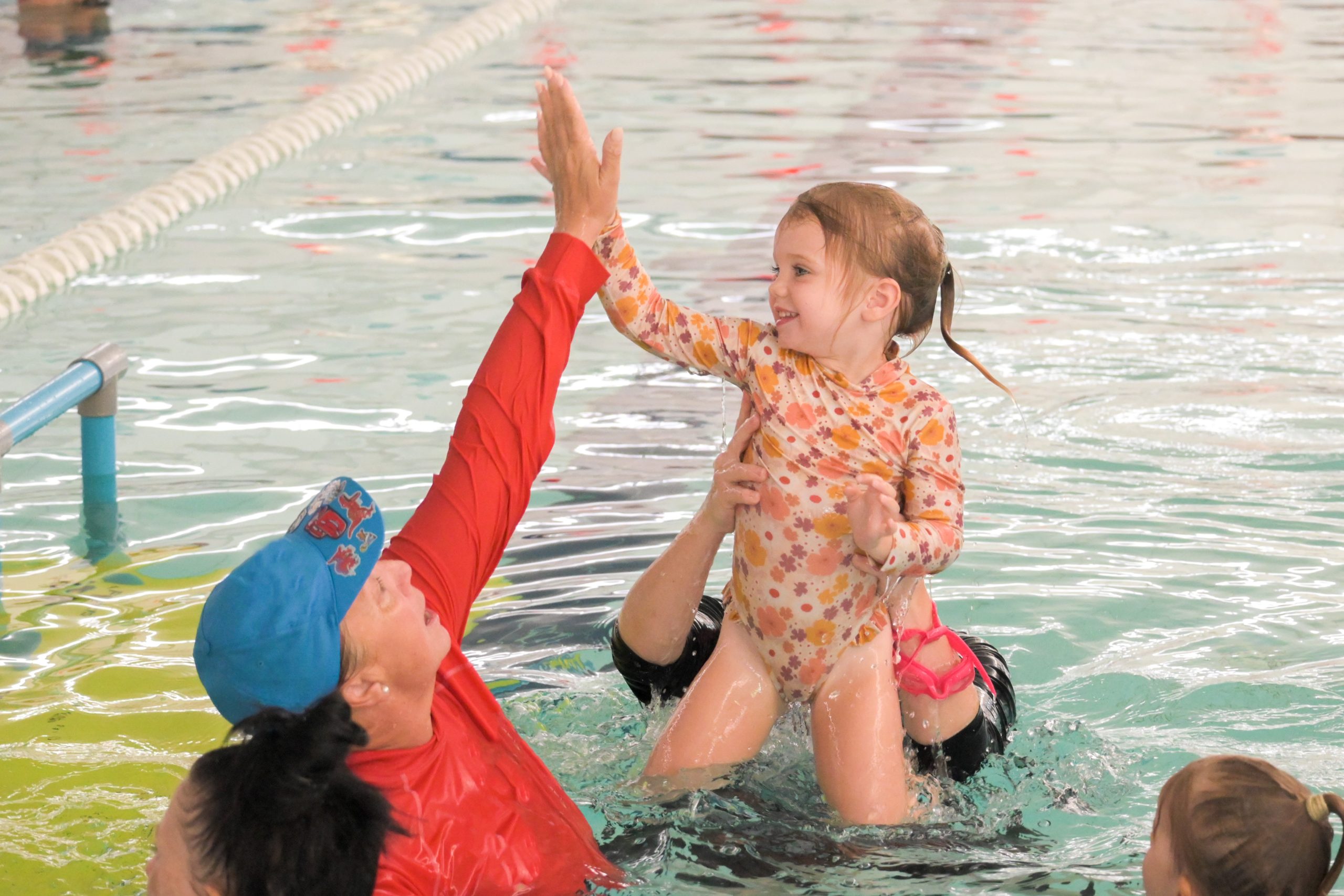 Instructor high fives young girl during swimming lesson